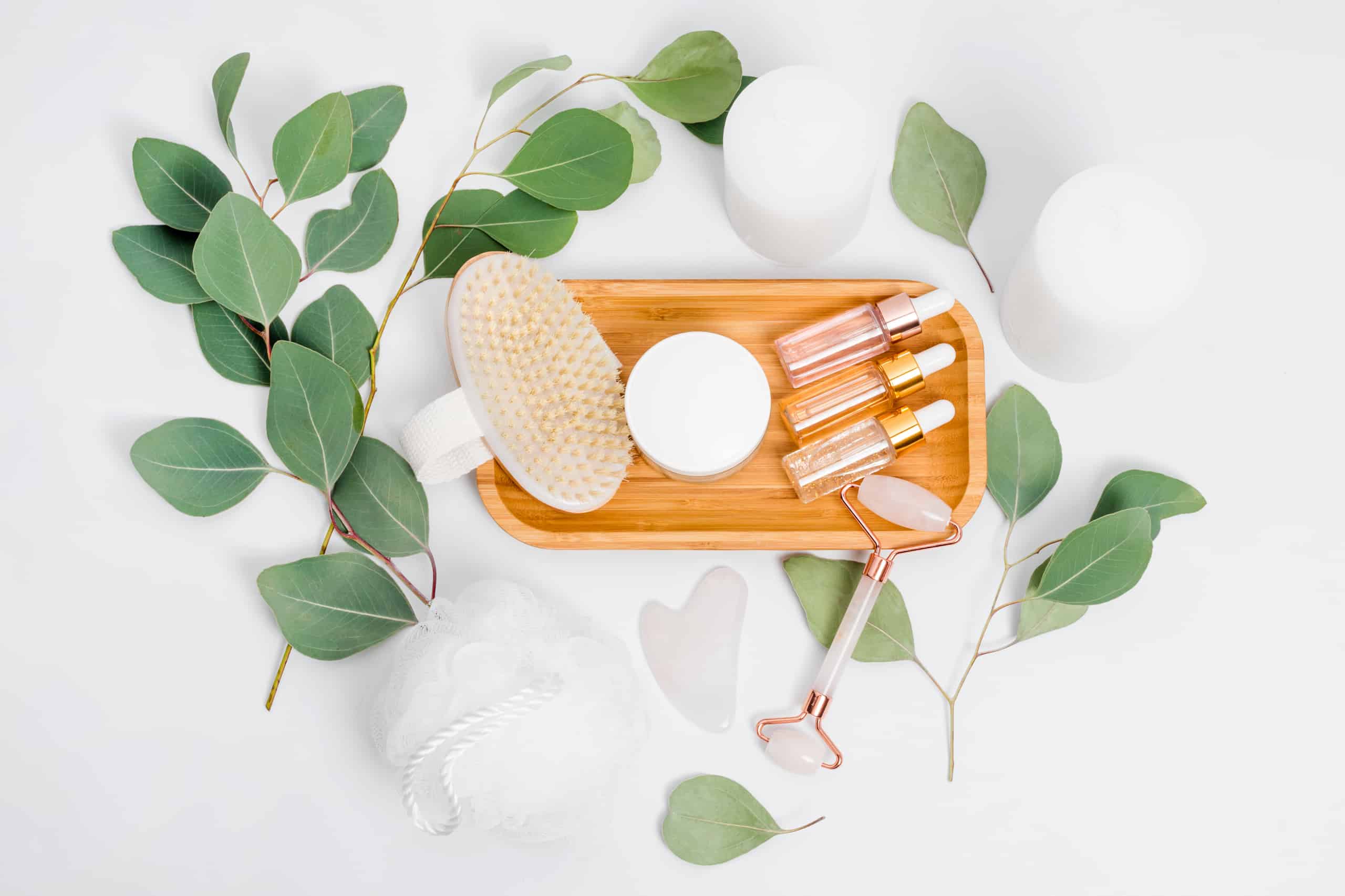 Facial roller, essential oils, cosmetic serums, massage brush and candles with natural eucalyptus leaves. Beauty products, massage tools, facial skin care, spa beauty treatment concept. Flat lay